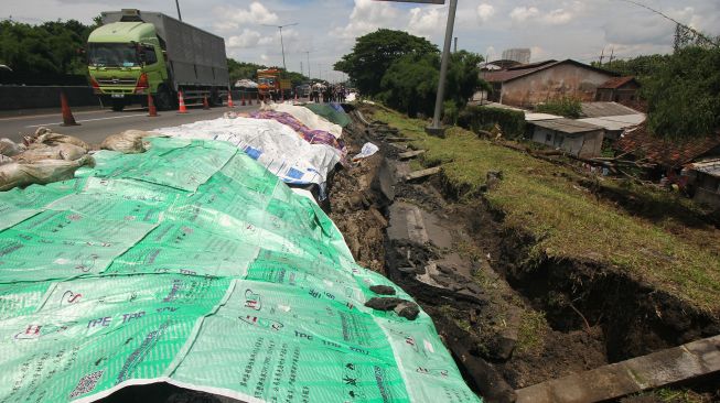 Sejumlah kendaraan melintas di dekat jalan tol yang longsor di ruas tol Surabaya-Gempol KM 06+200, di Surabaya, Jawa Timur, Rabu (27/1/2021).  [ANTARA FOTO/Didik Suhartono]