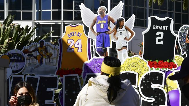 Sejumlah penggemar berkumpul di dekat sebuah poster dari mendiang pemain bola basket profesional NBA Kobe Bryant dan mendiang putrinya Gianna di pusat Kota Los Angeles, California, Amerika Serikat, Selasa (26/1/2021).  [Frederic J. BROWN / AFP]
