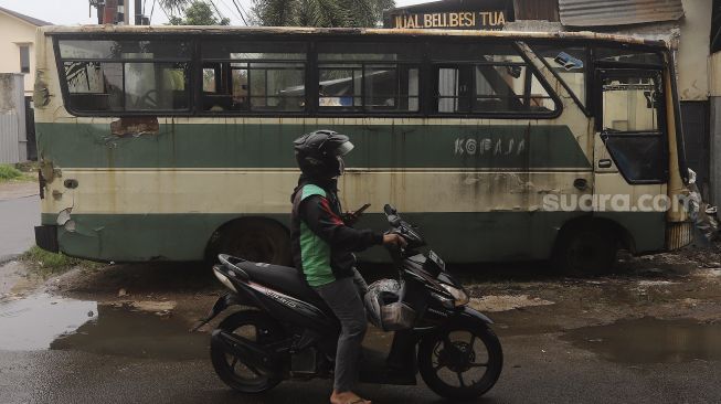 Pengemudi ojek daring melintas di samping bus Kopaja yang akan diremajakan di kawasan Meruya, Jakarta Barat, Rabu (27/1/2021). [Suara.com/Angga Budhiyanto]