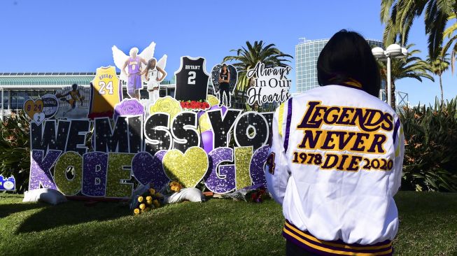 Sejumlah penggemar berkumpul di dekat sebuah poster dari mendiang pemain bola basket profesional NBA Kobe Bryant dan mendiang putrinya Gianna di pusat Kota Los Angeles, California, Amerika Serikat, Selasa (26/1/2021).  [Frederic J. BROWN / AFP]
