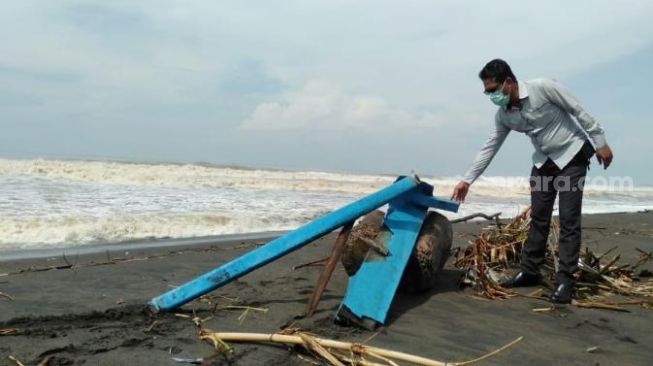 Anggota Polsek Kretek menunjukkan pecahan kapal jukung yang rusak dari insiden hilangnya penambang pasir di muara Sungai Opak, Bantul, Senin (1/2/2021). - (SuaraJogja.id/Muhammad Ilham Baktora)