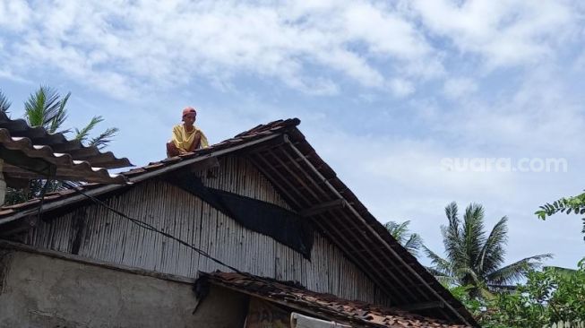 Warga Desa Rawa Boni, Paku Haji, Kabupaten Tangerang, tengah membetulkan genting rumah akibat terdampak angin puting beliung, Selasa (2/2/2021). [Suara.com/Muhammad Jehan Nurhakim]