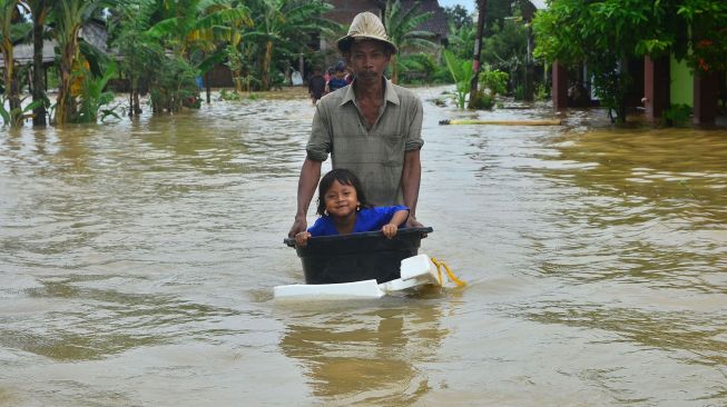 Warga membawa anaknya menggunkan ember melintasi jalan yang terendam banjir di Desa Kedungdowo, Kudus, Jawa Tengah, Selasa (2/2/2021).  [ANTARA FOTO/Yusuf Nugroho]
