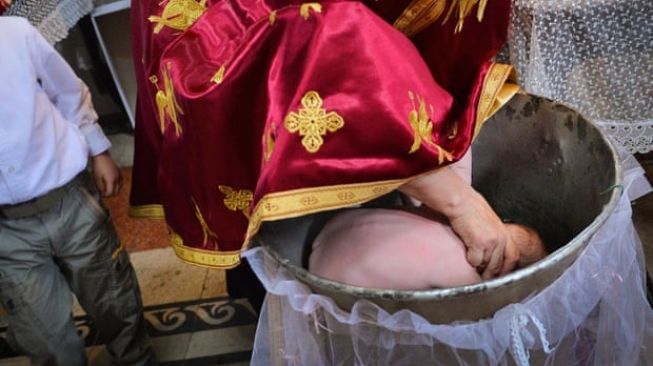  Imam ortodoks membenamkan seorang anak ke dalam air suci tiga kali selama pembaptisan.(Daniel Mihilescu / AFP / Getty Images)