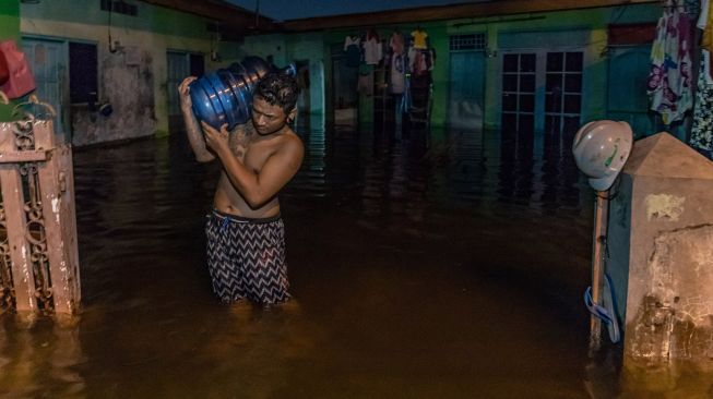 Seorang warga memikul galon air untuk kebutuhan air minum keluarganya yang mengungsi akibat banjir di Kelurahan Tanjung Mas, Semarang, Jawa Tengah, Sabtu (6/2/2021).  ANTARA FOTO/Aji Styawan