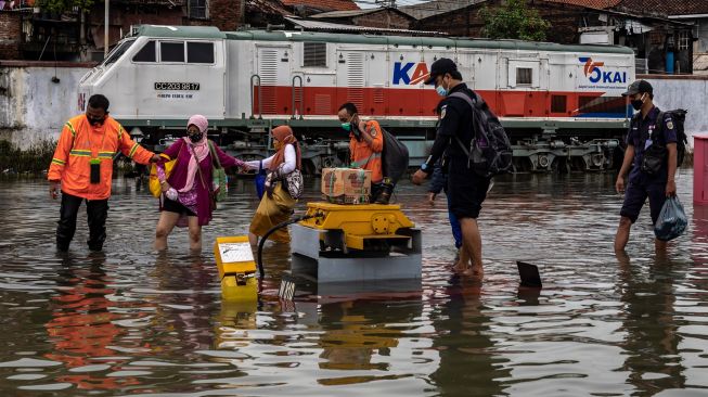 Karyawan membantu sejumlah penumpang menembus banjir untuk keluar dari Stasiun Tawang yang terendam banjir di Semarang, Jawa Tengah, Sabtu (6/2/2021). [ANTARA FOTO/Aji Styawan]
