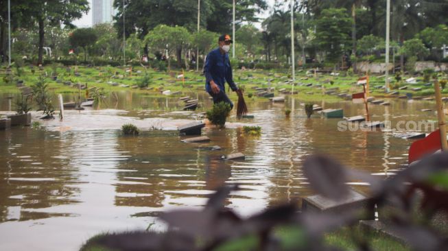 Petugas berusaha menyedot air di area pemakaman yang terendam banjir di TPU Karet Bivak, Jakarta Pusat, Minggu (7/2/2021). [Suara.com/Alfian Winanto]