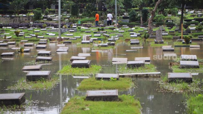 Warga melihat area pemakaman yang terendam banjir di TPU Karet Bivak, Jakarta Pusat, Minggu (7/2/2021). [Suara.com/Alfian Winanto]