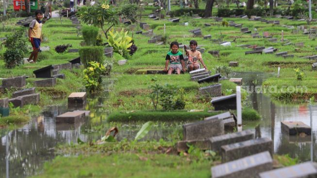 Anak - anak bermain di area pemakaman yang terendam banjir di TPU Karet Bivak, Jakarta Pusat, Minggu (7/2/2021). [Suara.com/Alfian Winanto]