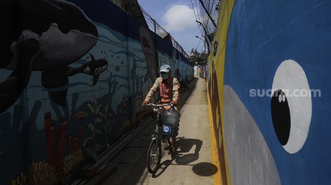 Seorang warga bersepeda melintas di depan mural bertema kehidupan laut di Kampung Lodan, Jakarta, Senin (8/2/2020). [Suara.com/Angga Budhiyanto]