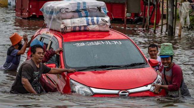 Sejumlah warga mendorong mobil mogok akibat menembus jalur Pantura Jalan Raya Kaligawe - Genuk yang terendam banjir di Genuk, Semarang, Jawa Tengah, Senin (8/2/2021). [ANTARA FOTO/Aji Styawan]