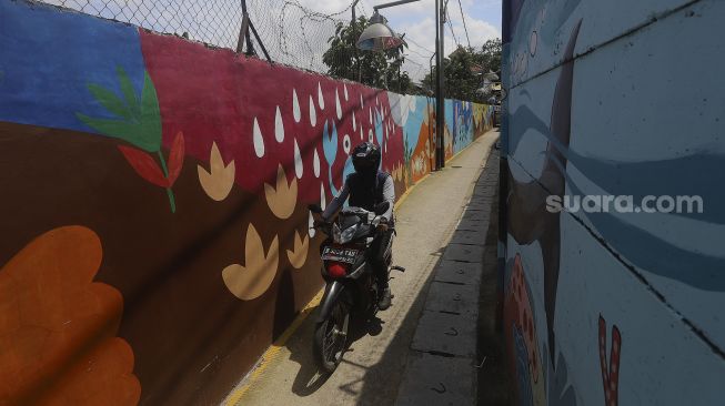 Pengedara sepeda motor melintas di depan mural bertema kehidupan laut di Kampung Lodan, Jakarta, Senin (8/2/2020). [Suara.com/Angga Budhiyanto]