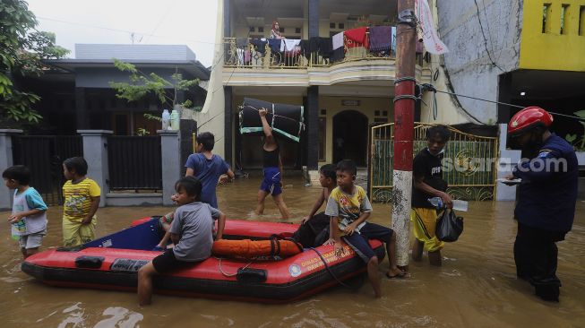 Sejumlah anak bermain di jalan yang tergenang banjir di kawasan Pejaten Timur, Pasar Minggu, Jakarta, Senin (8/2/2021). [Suara.com/Angga Budhiyanto]