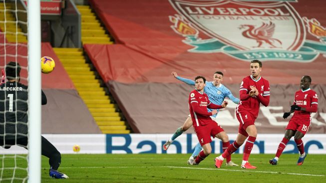 Gelandang Manchester City Phil Foden menendang bola ke arah kiper Liverpool Alisson Becker selama pertandingan sepak bola Liga Premier Inggris antara Liverpool melawan Manchester City di Stadion Anfield, Liverpool, Inggris, Senin (8/2/2021) dini hari WIB. Jon Super / POOL / AFP