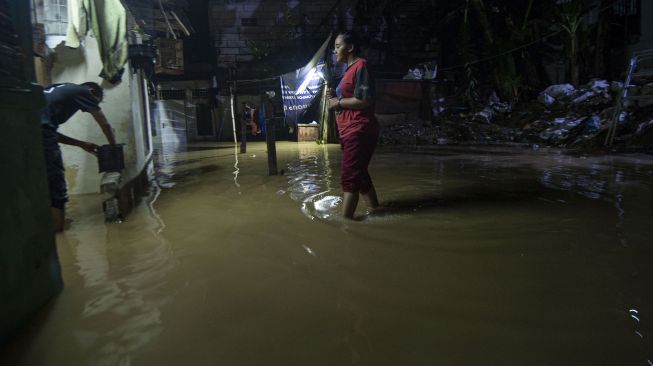 Warga melintasi banjir yang melanda lingkungan tempat tinggalnya di Pejaten Timur, Pasar Minggu, Jakarta, Minggu (7/2/2021). [ANTARA FOTO]
