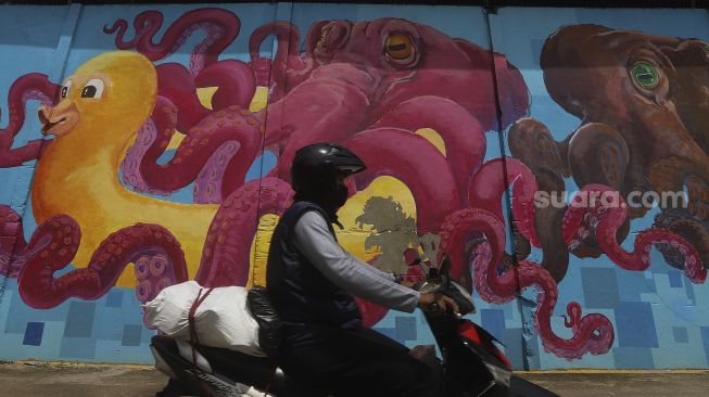 Pengedara sepeda motor melintas di depan mural bertema kehidupan laut di Kampung Lodan, Jakarta, Senin (8/2/2020). [Suara.com/Angga Budhiyanto]