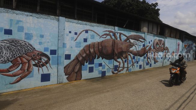 Pengedara sepeda motor melintas di depan mural bertema kehidupan laut di Kampung Lodan, Jakarta, Senin (8/2/2020). [Suara.com/Angga Budhiyanto]