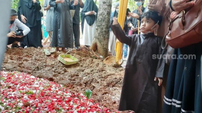 Salah satu balita putra Ustadz Maaher At-Thuwailibi ikut menabur bunga di pusara ayahnya usai dimakamkan di Pesantren Tahfiz Daarul Quran, Cipondoh, Kota Tangerang, Selasa (9/2/2021). [Suara.com/Wivy]