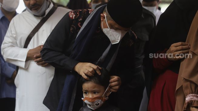 Ustadz Yusuf Mansur membetulkan masker yang dikenakan oleh anak pertama Almarhum Ustadz Maaher At-Thuwailibi saat prosesi pemakaman di Kompleks Pemakaman Pondok Pesantren Daarul Quran, Cipondoh, Tangerang, Banten, Selasa (9/2/2021). [Suara.com/Angga Budhiyanto]