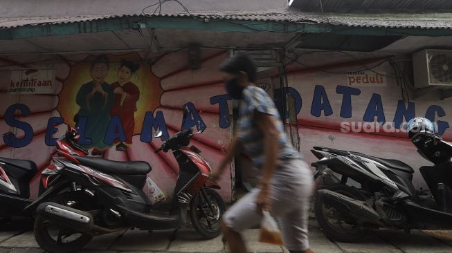 Warga berjalan di depan mural selamat datang di Kampung Tehyan, Kota Tangerang, Banten, Selasa (9/2/2021). [Suara.com/Angga Budhiyanto]