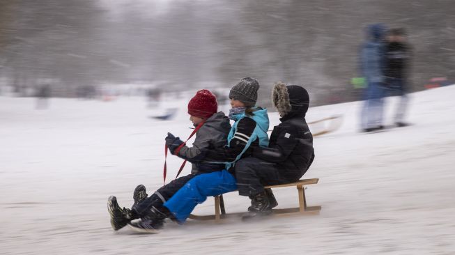 Anak-anak meluncur menuruni bukit dengan kereta luncur mereka di taman Wilmersdorf-Schoeneberg, distrik Schoeneberg, Berlin, pada (8/2/2021). [Odd ANDERSEN / AFP]