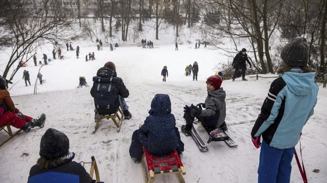 Anak-anak menunggu untuk meluncur menuruni bukit dengan kereta luncur mereka di taman Wilmersdorf-Schoeneberg, distrik Schoeneberg, Berlin, pada (8/2/2021). [Odd ANDERSEN / AFP]