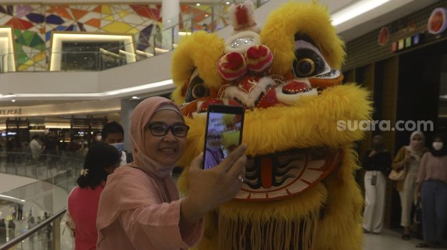 Seorang pengunjung berswafoto bersama Barongsai saat beraksi menghibur pengunjung dalam pertunjukan "Barongsai Spectacles" di Mal Senayan City, Jakarta, Jumat (12/2/2021). [Suara.com/Angga Budhiyanto]