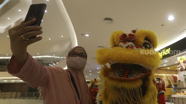 Seorang pengunjung berswafoto bersama Barongsai saat beraksi menghibur pengunjung dalam pertunjukan "Barongsai Spectacles" di Mal Senayan City, Jakarta, Jumat (12/2/2021). [Suara.com/Angga Budhiyanto]