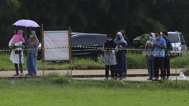 Keluarga memanjatkan doa saat menyaksikan dari kejauhan pemakaman jenazah korban COVID-19 di TPU Bambu Apus, Jakarta Timur, Sabtu (13/2/2021). [Suara.com/Angga Budhiyanto]