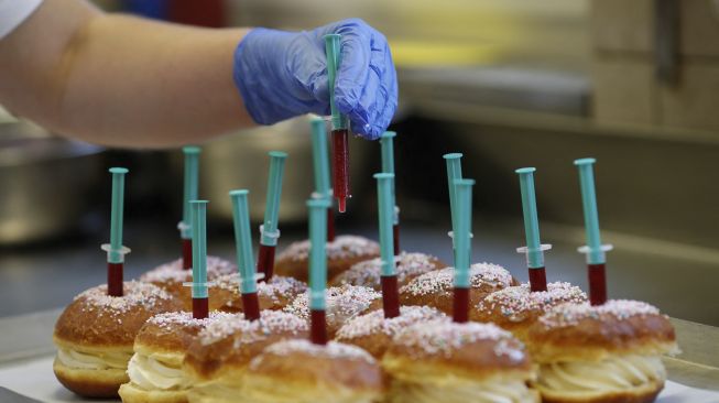 Seorang karyawan meletakkan jarum suntik penuh jeli raspberry di atas berliner (donat Jerman) di toko roti Kreyenbuhl, Muri, Swiss, pada (5/2/2021). [STEFAN WERMUTH / AFP]