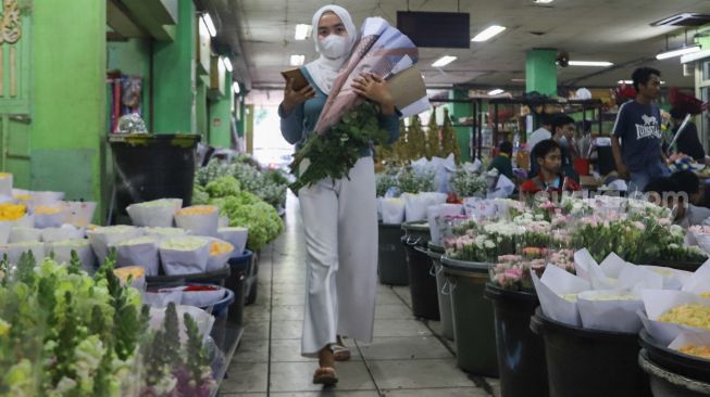 Pembeli membawa bunga yang dibelinya di Pasar Bunga Rawa Belong, Jakarta Barat, Minggu (14/2/2021). [Suara.com/Alfian Winanto]