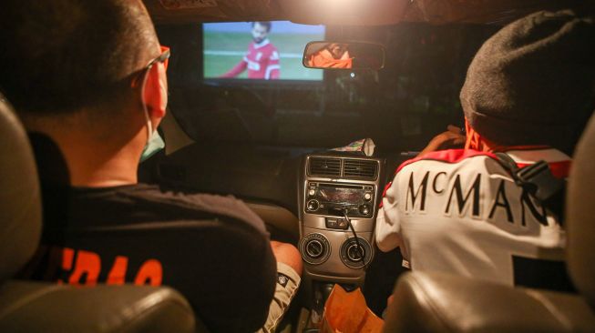 Dua orang pendukung salah satu tim sepak bola menyaksikan pemutaran pertandingan sepak bola dari dalam mobil di area parkir Mall Alam Sutera, Kota Tangerang, Banten, Sabtu (13/2/2021). ANTARA FOTO/Fauzan