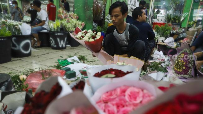 Pedagang membungkus bunga di Pasar Bunga Rawa Belong, Jakarta Barat, Minggu (14/2/2021). [Suara.com/Alfian Winanto]