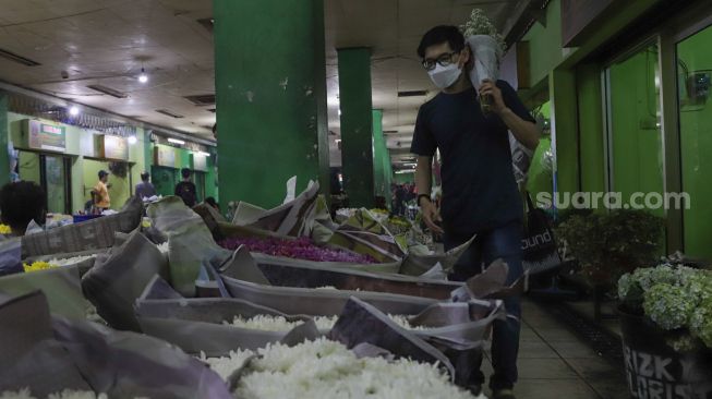 Pembeli membawa bunga yang dibelinya di Pasar Bunga Rawa Belong, Jakarta Barat, Minggu (14/2/2021). [Suara.com/Alfian Winanto]