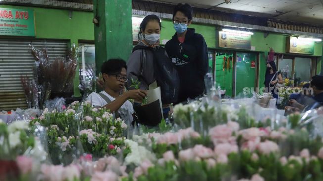 Pedagang membungkus bunga untuk pembeli di Pasar Bunga Rawa Belong, Jakarta Barat, Minggu (14/2/2021). [Suara.com/Alfian Winanto]