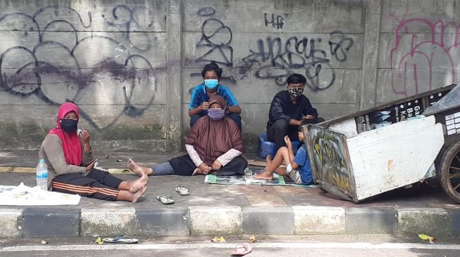 Rodiah dan Nengsih serta anak-anaknya yang menjadi keluarga pemulung tengah beriatirahat di depan SMA ora Et Labora di Jalan Angsana, Rawa Buntu, Serpong, Kota Tangsel, Senin (15/2/2021). [Suara.com/Wivy Hikmatullah]