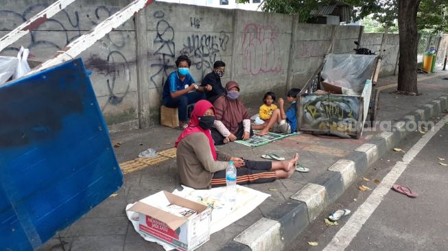 Rodiah dan Nengsih serta anak-anaknya yang menjadi keluarga pemulung tengah beriatirahat di depan SMA ora Et Labora di Jalan Angsana, Rawa Buntu, Serpong, Kota Tangsel, Senin (15/2/2021). [Suara.com/Wivy Hikmatullah]