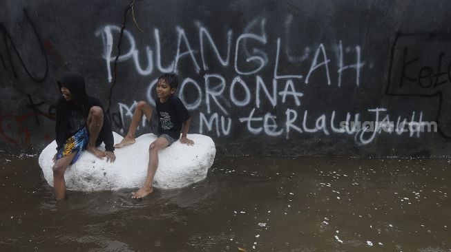 Dua anak bermain menggunakan styrofoam saat banjir merendam kawasan Kemang Utara, Jakarta, Kamis (18/2/2021). [Suara.com/Angga Budhiyanto]