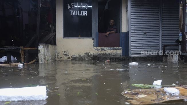 Seorang warga duduk di salah satu kios saat banjir merendam kawasan Kemang Utara, Jakarta, Kamis (18/2/2021). [Suara.com/Angga Budhiyanto]