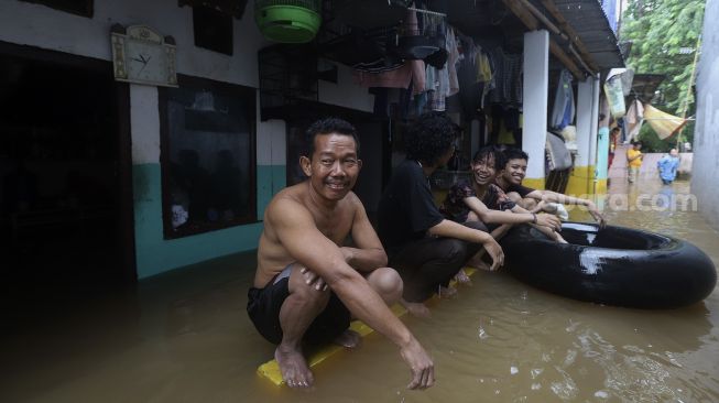 Warga beraktivitas di depan rumahnya yang terendam banjir di Cipinang Muara, Jakarta, Jumat (19/2/2021). [Suara.com/Angga Budhiyanto]