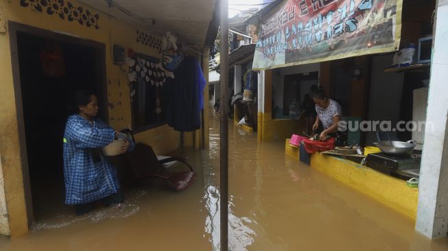 Warga memasak di rumahnya yang terendam banjir di Cipinang Muara, Jakarta, Jumat (19/2/2021). [Suara.com/Angga Budhiyanto]