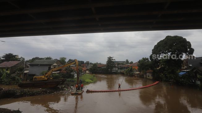 Petugas UPK Badan Air Kecamatan Makasar dibantu alat berat melakukan pengerukan sampah di Kali Sunter, Kelurahan Cipinang Melayu, Jakarta, Jumat (19/2/2021). [Suara.com/Angga Budhiyanto]