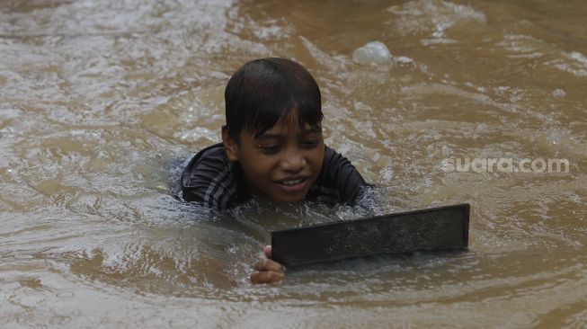 Seorang anak bermain air saat banjir merendam Kelurahan Cipinang Melayu, Jakarta, Jumat (19/2/2021). [Suara.com/Angga Budhiyanto]