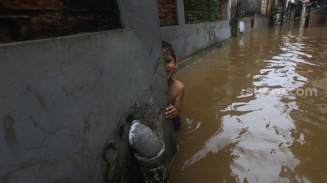 Seorang anak bermain di dekat rumahnya yang terendam banjir di Cipinang Muara, Jakarta, Jumat (19/2/2021). [Suara.com/Angga Budhiyanto]