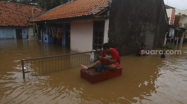 Warga beraktivitas saat banjir merendam Kelurahan Cipinang Melayu, Jakarta, Jumat (19/2/2021). [Suara.com/Angga Budhiyanto]