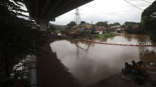 Sejumlah warga menyaksikan proses pengerukan sampah di Kali Sunter, Kelurahan Cipinang Melayu, Jakarta, Jumat (19/2/2021). [Suara.com/Angga Budhiyanto]