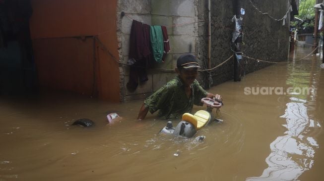 Seorang warga berjalan melintasi banjir yang merendam Kelurahan Cipinang Muara, Jakarta, Jumat (19/2/2021). [Suara.com/Angga Budhiyanto]