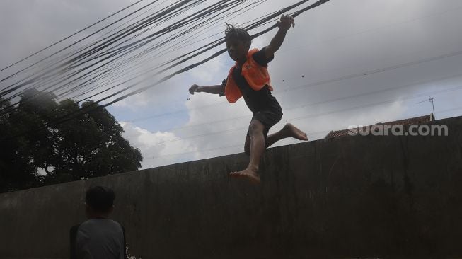 Seorang anak melompat ke air saat banjir merendam Kelurahan Cipinang Melayu, Jakarta, Jumat (19/2/2021). [Suara.com/Angga Budhiyanto]