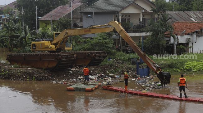 Petugas UPK Badan Air Kecamatan Makasar dibantu alat berat melakukan pengerukan sampah di Kali Sunter, Kelurahan Cipinang Melayu, Jakarta, Jumat (19/2/2021). [Suara.com/Angga Budhiyanto]