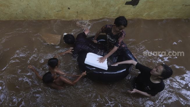 Sejumlah anak bermain air saat banjir merendam Kelurahan Cipinang Muara, Jakarta, Jumat (19/2/2021). [Suara.com/Angga Budhiyanto]